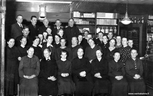 Diakoniaompeluseura
Diakoniaompeluseura on kokoontunut kirkonkylän KPO:lla ja Otto Junnola on käynyt ottamassa kuvan. 
Takana seisomassa 1. oikealta "Aari" Adrian Lähdevirta (alk. Källström, Nuottila 5), Kälviän seurakunnan pitkäaikaisen lukkarin Matti Källströmin poika. Aari toimi mm. urkujenpolkijana, posteljoonina sekä kuului vieraana "vakituiseen kalustoon" kinkereillä, hautajaisissa jne. Takana 1. vas. kirkkoherra Johannes Kaukovaara (1887-1958, Simukkala 15), 3. Jalmari Huhtala. 
Heidän alapuolellaan vas. Kalle Hyyppä, miesten edessä takana sisarukset Kaino Koittola ja Anna Koittola (Penttilä 41). 
Toisessa rivissä 2. vas. Mandi Kuhanen, 3. Rauha Marttila, 4. Nasto Laine (Kesäniemi 2), 6. Iida Nurila (Nurila 27) ja 7. opettaja Lempi Huhtala.
Kuvassa ovat mahdollisesti myös KPO:n kaupanhoitaja Kalle Nissi ja Kaukovaaran vaimo, Ida Kaukovaara. 

Johannes Kaukovaara oli kappalaisena Kälviällä vuosina 1917-1927 ja muutti sen jälkeen Nousiaisiin. Vuonna 1936 hänet valittiin kirkkoherraksi ja sitä virkaa hän hoiti Kälviällä kuolemaansa saakka.

Jos tunnistat kuvan henkilöitä, lähettäisitkö tietoja sähköpostitse osoitteeseen vanhat.kuvat@vanhakalvia.fi  Kiitos avustasi!
Keywords: Nissi Kaukovaara Hyyppä Junnola Koittola Kuhanen Marttila Laine Nurila Huhtala Källström Lähdevirta  