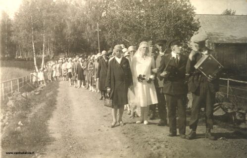 Hääkulkue Kälviällä
Vietetään Martta ja Urho Ahon häitä. Pelimannit kulkevat vihkiparin edellä ja muu väki seuraa perässä.
Viulupelimanni on joko Toivo tai Valpas Pykälämaa. 

Missä kulkue on kuvattu? Vaatemuodin perusteella häät on pidetty 1920-luvulla.
Kuva voi liittyä Palon sukuun. Jos tiedät jotain kuvaan liittyvää, ota yhteyttä tai kirjoita tiedot kuvan alle kommenttikenttään. Kiitos avustasi!
Keywords: Aho Pykälämaa 
