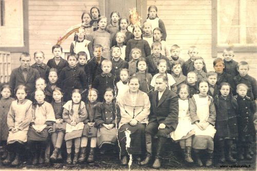 Välikylän koululaisia 1924-1925
Kuvassa ainakin Palon lapset Liina s. 1911, Matti s. 1913 ja Toini s. 1915 (Palo 8)
Liina, ylärivissä 2. oikealta, on raaputtanut omat kasvonsa pois kuvasta, Matti on 2. vasemmalta kolmannessa rivissä ja Toini 6. vasemmalta eturivissä. 
Eturivissä 3. oik. Hilda Kotkajuuri (s. 1914) ja  2. rivissä opettajien välissä, tumma tukka ja pusero Hellin Kotkajuuri (s.1917, Hietakangas 4). Eturivissä 1. oikealta Lempi Huhta (s. 1917, myöh. Maunula, Huhta 18).
Alhaalta päin toisessa rivissä vasemmalla Pajalan Pauli (s. 1911, Pajala 19), hänestä oikealla poika, jonka pää näkyy, Pasanterin Martti eli Martti Maunula. Toisessa rivissä oikealta 4. Uuno tai Urho Tikkanen. 
Alhaalta päin kolmannessa rivissä oikealta 2. mahdollisesti Martti Ruokoja (s. 1911, Ruokoja 22) ja samassa rivissä oikealla 4. on ehkä Satokosken poikia. Uuno Rautomäki (s. 1911) on neljännessä rivissä alhaalta päin, 4. oikealta, hieman pidempi vierustovereita. Helli (s. 1913) ja Ensti (s. 1915) Rautomäki saattavat olla kuvassa.  Ylimmässä rivissä 3. oikealta mahdollisesti Aino Ruokoja (s. 1913, o.s. Herlevi, Rimpioja 24). 
Edessä istuu koulun opettajapariskunta, Tyyne (o.s Ahola, s. 1893) ja Kaarlo eli Kalle Väre (s. 1889 Jämsä). He tulivat Kälviälle 1924  Kuhmalahdelta ja olivat Välikylän koulun opettajina vuoden. Kälviältä he siirtyivät Alavudelle. Heillä oli tytär Anna-Liisa (s. 1922). Kalle Väre toimi myös Evankeliumiyhdistyksen maallikkosaarnaajana. Kirkonkirjoissa mainitaan, että hän on pitänyt seuroja Välikylän koululla.
Monta lasta vielä tunnistamatta. Jos tunnistat heitä, ottaisitko yhteyttä! 
Keywords: Palo Pajala Maunula Satokoski Rautomäki Huhta Maunula Tikkanen Kotkajuuri Ruokoja Herlevi Ahola Väre Kuhmalahti Alavus Hilli Välikylä