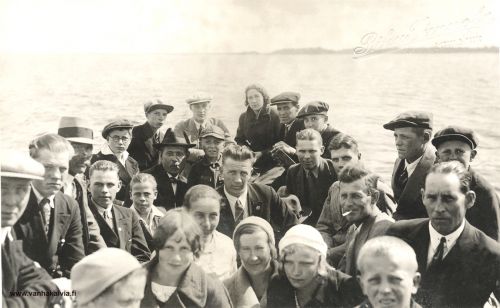 Kesäjuhlilla 
Kuva on todennäköisesti otettu Rytikarilla, kesäjuhlien aikana. Taustalla näyttäisi olevan Junnilanperän ranta. Vene on mahdollisesti Junnilan veljesten vene, ja he ovat mukana kyydissä. Silmälasipäisen pojan, Junnilan Paavon, oikealla puolella oleva hattupäinen mies on yksi näistä veljeksistä, Riku Junnila (s. 1894). Toinen veli Väinö Junnila (s. 1900)  on keulassa istuvan Tyyne Järven oikealla puolella. Kolmas veljeksistä on Ensti Junnila (s. 1900) ja on oikeassa laidassa etummaisena, kravatti kaulassa ilman hattua. Junnilan veljekset (Kinnari 24). 
Riku Junnilan oikealla puolella oleva poika on mahdollisesti Leevi Junnila. Ensti Junnilan takana oleva poika mahd. Oiva Pietilä (Pietilä 30).

Etualalla olevista tytöistä vasemmalla Esteri Hakunti (m. Pietilä, Hakunti 21), hänen takanaan oikella puolella vaaleapuseroinen Anna Järvi (s. Sandström, Järvi 28), Helli Uusimäki (m. Hillilä, Uusimäki 1) ja oikealla on Lempi Hakunti (vaaleat hiukset) (Hakunti 21). Anna Järvestä oikealla on mahd. joku Lahden veljeksistä (Kinnari 27, Lahti). Anna Järven vasemmalla puolella oleva nuorin poika on Mauno Junkkila. Silmälasipäinen poika on Paavo Junnila ja hänen takanaan oleva toinen lippalakkipäinen poika on Usko Lahti (Kinnari 27, Lahti).

Keulassa oleva nainen on Tyyne Järvi (Järvi 25). Hänestä oikealla reunalla on kaksi miestä, joista nuorempi on Valto Valkama (leuka piilossa) (Valkama 17). Samalla reunalla, Valtosta seuraava lippalakkipäinen mies on Kaino Palola. Tupakki suupielessä oleva mies oikealla keskellä on Valdemar Toivonen, Karikkaan vävy (Karikka 24).

Vasemmalla laidalla arvellaan olevan joku Hakuntin "Janneksen pojista", mahdollisesti Arvo (Hakunti 23). Hänen takanaan on mahd. joku Nissilän veljeksistä (Nissilä 22).

Keywords: Hakunti Pietilä Järvi Sandström Uusimäki Hillilä Junkkila Junnila Järvi Valkama Palola Toivonen Karikka 