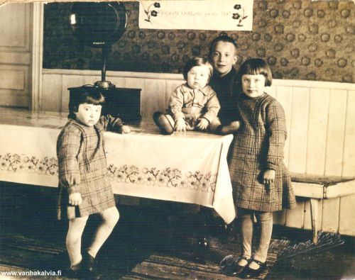 Riihimäellä 
Riihimäen tuvassa vas. Eeva, Kalle (pienin), Antti ja Maiju Riihimäki. 
Lasten vanhemmat olivat Antti Emil ja Ellen Riihimäki (Riihimäki 13, Matinjussi 19).

Huomaa komea gramofoni ja huoneentaulun teksti ”Vain unta haihtuvaa on elo tää”.

Keywords: Riihimäki 