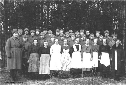 Kälviän suojeluskunnan voimistelukurssi 1925
Kälviän SK:n voimistelukurssi pidettiin Ruotsalolla 23.-25.1.1925. Vasemmalla yliesikunnan urheiluosaston päällikkö, kapteeni Levälahti. Oikealla piirin urheiluohjaaja Sammallahti ja paikallispäällikkö Asujamaa.
Edessä 2. vas. seisova nainen on "Matjussin mamma" Hilma Johanna Paasiala (1863-1938). Hänen vieressään vaaleissa vaatteissa on Tyyne Rimmi ja seuraava oik. Lempi Lehto. Oikealta 4. on Impi Kippo ja 3. oikealta Anna Kippo. Oikeassa reunassa, takki yllään Hilma Porko.
Keskirivissä, oikealta  3. Verner Karhulahti (?), 4. oikealta Lahden veljeksiä ja 5. oikealta on Armas Hakunti. 
Takarivissä 3. vas. Toivo Kuusiniemi, 4 vas. Pentti Vähälä, 5 vas. Aatu Järvi, 9. vas. Martti Karhulahti, 10. vas. Pauli Rimmi (näkyy vain osa kasvoista). 
Edessä (naisten takana) 4. oik Toivo Lahti, 3. oik mahd Fritiof Karhulahti, Lauri Porri Tyyne Rimmin ja Lempi Lehdon välissä takana. Kapteeni Levälahden vieressä Viljo Kippo.

Keywords: Levälahti Sammallahti Asujamaa Rimmi Matinjussi Paasiala Lehto Kippo Porko Karhulahti Lahti hakunti Järvi 