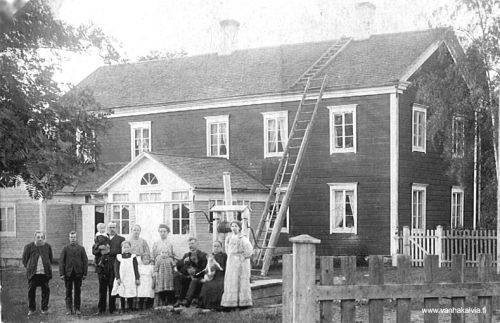 Tobias Heikkilä Lohtajalla
Kuva on Lohtajalta, Koivuluodosta (nyk. Mattila), jossa Tobias Heikkilä (vasemmalla) (Heikkilä 16) eli viimeiset vuotensa. 
Talon omisti neiti Snellman, Vetelin papin tytär, joka istuu kuvassa koira sylissä.
Koivuluoto oli kestikievari ja neiti Snellman huolehti kunnan huonompiosaisista. Tobias Heikkilä  asui jonkin aikaa Koivuluodon vintissä ja myöhemmin hänellä oli pihapiirissä pieni tupa, jonka kivijalka vielä on jäljellä. Tobiaan pikkutupa on siirretty kirkon lähelle Mikko Uusitalon pihapiiriin.
"Vapaaherra" Antti Heikkilä oli Tobiaksen poika. 
Kuvassa vasemmalla Tobias Heikkilä. Seuraavana luultavasti Matti Puukangas (Fröökynän renki) ja Jooseppi Vähähyyppä sylissä poikansa Otto, Hilma Vähähyyppä (s. Huhtala), Eeva Maria Kippo ja Aadolf Kippo istumassa kaivon kannella, kaivon kannella myös Fröökynä Ida Snellman, oikealla Fröökynän keittiöpiika Iida Rita Alavieskasta (myöhemmin Janne Erkkilän vaimo). Edessä lapset Vieno Kippo, Tyyne Kippo, Siikri Vähähyyppä. 
Kuva on otettu 1910, kun Kippo ja Vähähyyppä ostivat Koivuluodon Fröökynältä.
Tobias asui läheisellä Taxsellin mäellä, mutta kun hänen vaimonsa kuoli, niin luultavasti Fröökynä on huolehtinut hänestä.
Keywords: Heikkilä Matinjussi Koivuluoto Snellman Lohtaja Mattila Kippo Vähähyyppä Rita Alavieska Erkkilä Veteli  