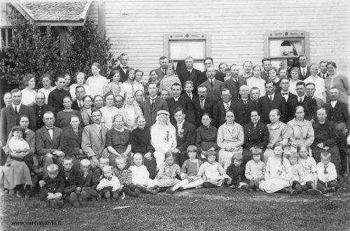 Hääjuhla Ruokojalla
Hääkuva on Ruokojalta ja tapahtuman ajankohta 24.6.1926. Vietetään Lyyli Lehdon (s. 1897, Pietilä 25) ja Otto Ruokojan (s. 1896, Ruokoja 19) häitä. Vanhan Kälviän galleriassa on tästä tilaisuudesta toinenkin kuva: Häät Ruokojalla. 
Morsiamen vieressä istuu hänen äitinsä Edla Sofia Lehto (s. Ingalsuo 1860-1945) ja sulhasen vieressä äitinsä Anna Sofia Ruokoja (1854-1934). Pappi on Johannes Kaukovaara ja pitkä mies hänen vieressään näyttäisi olevan Aatu Valkama (Valkamaa 16), joka mahdollisesti on toiminut kanttorina, vierellään vaimonsa Lempi (s. Kippo). Miesten takana näkyy Vilhelmiina Huhta (s. Hakunti, Huhta 18). Vilhelmiinasta vasemmalle samassa rivissä ovat Kustin Hanna eli Hanna Aho (Huhtan mäkitupa) ja Ollikaisen Selema (Ruokasalo 6).
Lasten takana toinen vasemmalta on Kalle Huhta (Huhta 14/16), hänen oikealla puolellaan vaimo Loviisa (Ruokoja 20) Lapsista toinen vasemmalta on Pasanterin Martti eli Martti Maunula (Maunula 22). Kolmannella rivillä vasemmalta henkilö, jolla on musta paita ja valkoiset napit, on Ahlskogin vanha isäntä eli Matts Leander Ahlskog (Maunula 20). Ahlskogin isännästä oikealle, ensimmäinen pitkä mies tummassa puvussa, on Jannes Ruokoja eli Olli (Ruokoja 22) ja hänen oikealla puolellaan näkyy Lyyti-vaimon pää (Huhta 14). 
Ylhäällä vasemmanpuoleisen ikkunan vasemmalla puolen on Tirehtööri Antti eli Antti Salo (Hilli 18). 
Oikeanpuoleisen ikkunan oikealla puolella on morsiamen veli Edi Edvart Lehto (Pietilä 25). Olisiko saman ikkunan vasemmalla puolella rusetti kaulassaan Jarl Ingalsuo (Ingalsuo 28) vai onko hän Martti Ruokoja (Ruokoja 22)?
Jos tunnistat kuvan henkilöitä, lähettäisitkö tietoja osoitteeseen  vanhat.kuvat@vanhakalvia.fi
Kiitos avustasi!
Keywords: Ruokoja Lehto Kaukovaara Valkama Huhta Maunula Ahlskog Salo Aho Ollikainen Ingalsuo 