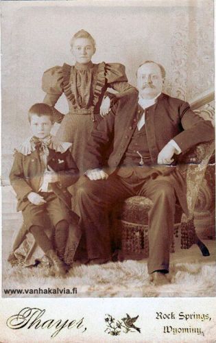 Adolf Riippa perheineen
Kuvassa Adolf Riippa (1855-1911, Riippa 18), hänen suomalaissyntyinen vaimonsa May sekä vuonna 1889 syntynyt Elmeri-poika. Adolf oli ylioppilas, luki jumaluusoppia 1878-82 Helsingin yliopistossa ja opiskeli sitten pari vuotta historiallis-kielitieteellisessä tiedekunnassa. Adolf otti työkseen kotimaakuntansa muinaisjäännösten inventoinnin, mutta opinnot sujuivat hitaasti ja työ jäi kesken. Hän toimi myös vt. lehtorina Kokkolan alkeiskoulussa.
Adolf päätti lähteä Amerikkaan vuonna 1892, mutta juhli ystävien kanssa niin pitkään, että laiva oli jo irti laiturista, kun vossikka toi häntä satamaan. Hetkeäkään epäröimättä Adolf hyppäsi mereen ja ui laivan kylkeen, mistä hänet nostettiin laivaan. Tapahtuma oli aiheena Juhani Ahon lastussa ”Hyppäys toiseen maailmaan”.
Amerikassa Adolf Riippa valmistui papiksi, toimi Suomi-Synodin palveluksessa monissa suomalaisseurakunnissa vihkien ja kastaen siirtolaisia ja heidän lapsiaan. Asuinpaikkoja ovat olleet ainakin Rock Springs, Wyoming ja Astoria, Oregon. 
Adolf kävi vuonna 1909 kotimaassa. Hän kuoli 1911 ja on haudattu Deep Riverin hautausmaahan. 
Keywords: Riippa RockSprigs Wyoming Astoria Oregon DeepRiver Washington USA