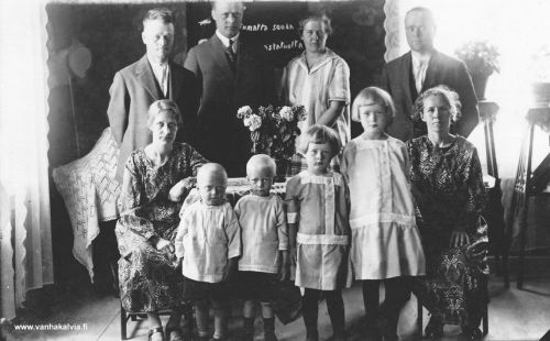 Laineen veljekset perheineen
Vasemmalla reunalla Mari ja Mikko Laine ja edessä pojat Väinö (s. 1922) ja Pauli (s. 1923) (Komosalo 5). Oikealla reunalla Pekka ja Nasto Laine sekä tyttäret Anni (s. 1918) ja Maiju (s. 1921) (Kesäniemi 2). Keskellä on Pauli Laine Tyyni-vaimonsa kanssa. 
Veljekset olivat syntyneet Vuokkiniemessä. Mikko ja Pekka liikkuivat kauppiaina mm. Kälviällä. He osallistuivat Vienan kansannousuun ja pakenivat Suomeen ja perheet muuttivat Kälviälle. 
Seinävaatteessa teksti: "Sortumatta souda vaikk ois vastatuulta." 

Keywords: Laine Vuokkiniemi 