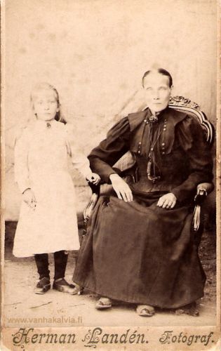 Maria Helena Rinell ja tytär Elsa Maria
Maria Helena Rytikangas eli Rinell s. Kronholm syntyi Lohtajalla 1.8.1853. Marian vanhemmat olivat Johan Hansson Kronholm ja Greta Matsdotter Domars. Perhe oli ruotsinkielinen ja kotoisin Kokkolan maaseurakunnasta Kaarlelasta. Kronholmit olivat vuokranneet Marinkaisista entisen sotilasvirkatalon Kipon. Heille syntyi 11 lasta, jotka aikuisikään vartuttuaan muuttivat pois Lohtajalta. Vanhukset Johan ja Greta kuolivat itsellisinä Marinkaisissa.
Maria Kronholm ja Salomon Rytikangas vihittiin Viipurissa. Maria oli tullut lapsenpiiaksi veljelleen ja Salomon tuli työhön Marian veljelle, joka urakoi rakennustyömailla. Perhe asui Viipurin Kolikkoinmäellä. Perheeseen syntyi kaksi lasta Juho Leonard s.8.6.1880 ja Elsa Maria s.21.2.1893. Poika Leonardilla ei ollut jälkikasvua. Sen sijaan tytär Elsa avioitui Olavi Parviainen -nimisen miehen kanssa ja heille syntyi yksi tytär Irja Annikki 19.2.1917. 
Rinellien koti tuhoutui vuonna 1918, kun Karjalan joukkojen komentaja everstiluutnantti Sihvo valloitti Viipurin. Elsa Parviainen muutti vuonna 1928 leskenä Hyvinkäälle mukanaan Irja-tytär. Suku jatkuu Hyvinkäällä Irja Suvensalmen (s. Parviainen) avioliiton myötä. 
Kun kuvaa suurentaa, siinä näkyy kolmaskin perheenjäsen. Maria Helenan hameenhelman alle on piiloutunut pieni koira.
Keywords: Rytikangas Rinell Parviainen Suvensalmi Viipuri Hyvinkää Kronholm Lohtaja 