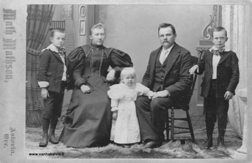Andersonin perhe Astoriassa 
Kuvassa Juho Viljami Matinjussi (1863-1932, Matinjussi 19) ja Maria Lyydia Lillkåla (Ostrom, Uusitalo) (1863-1919, Uusitalo 13)  kolmen lapsensa kanssa. Perhe käytti sukunimeä Anderson. 
John William Anderson ja Lydia Ostrom vihittiin avioliittoon Astoriassa, Oregonissa 20.8.1885. Kuva on otettu 1890-luvun puolivälin jälkeen, ehkä 1897. Kuvassa ovat pojat Einar William (1886-1949) ja Carl Fritiof (1887-1908) ja luultavasti  tytär Helmi Melida (1894-1910). Vuonna 1889 syntynyt tytär Helmi Lydia kuoli kurkkumätään kolmivuotiaana 1892 ja hänen jälkeensä syntyneet pojat George Waino (1891-1892) ja Hugo Nestor (1893) kuolivat aivan pieninä. Myös nuorimmat tyttäret Aune Ellen (1898-1917) ja Meva Etna Laila (1901-1917) menehtyivät nuorina. Ainoastaan perheen esikoinen Einar William varttui aikuiseksi ja eli vanhuuteen saakka. 
Kuvan takana on teksti: Matjussin Antin poika perheineen. Kuvan alalaidassa lukee vielä erikseen: Lyyti Uusitalo
Keywords: Anderson Astoria Oregon USA Matinjussi Lillkåla Ostrom Uusitalo