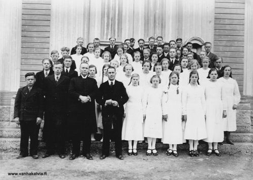 Rippikoululaiset 1939
Kuvan takana on päivämäärä 7.5.1939. Henkilöistä on tunnistettu Kälviän kirkkoherra Johannes Kaukovaara (1887-1958, Simukkala 15) (miehistä keskimmäinen) ja alhaalta päin toisessa rivissä kolmantena oikealla oleva, vaaleatukkainen Saara Sofia Hirvi (s. 1923, o.s. Hakunti, Hakunti 21).  Toisessa rivissä täältä kahtottuna Kaukovaaran oikialla pualella on Katri Hilli (myöh. Pajari, Hilli 26) ja Katrista oikialle käsin kolomas on Palon Elsa (myöh. Rautio, Palo 8). Kolmannessa rivissä alhaaltapäin, neljäs tyttö oikealta on Elli Kippo (s. 1922, Palomäki 2). Hänellä on polkkatukka, pinni vasemmalla. Jos tunnistat muita, lähettäisitkö tietoja osoitteeseen vanhat.kuvat@vanhakalvia.fi Kiitos avustasi!
Keywords: Kaukovaara Hirvi Hakunti Kippo Palo Rautio Pajari 